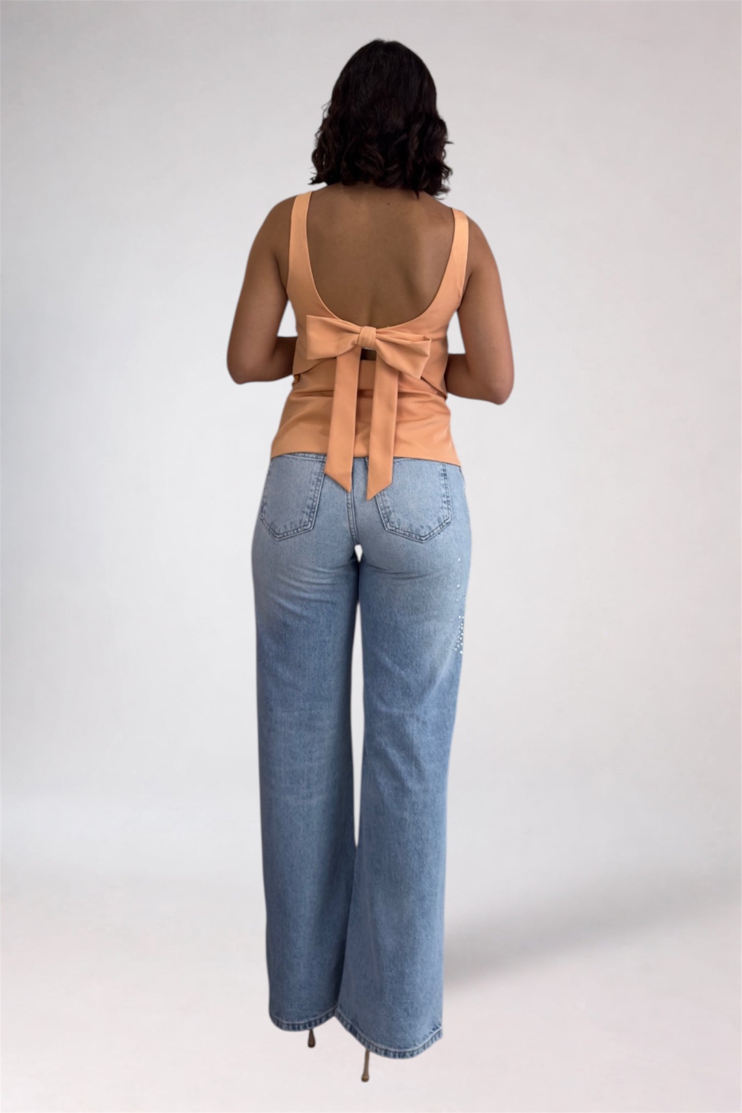 Woman wearing a beige sleeveless top with a bow and light blue jeans on a white background