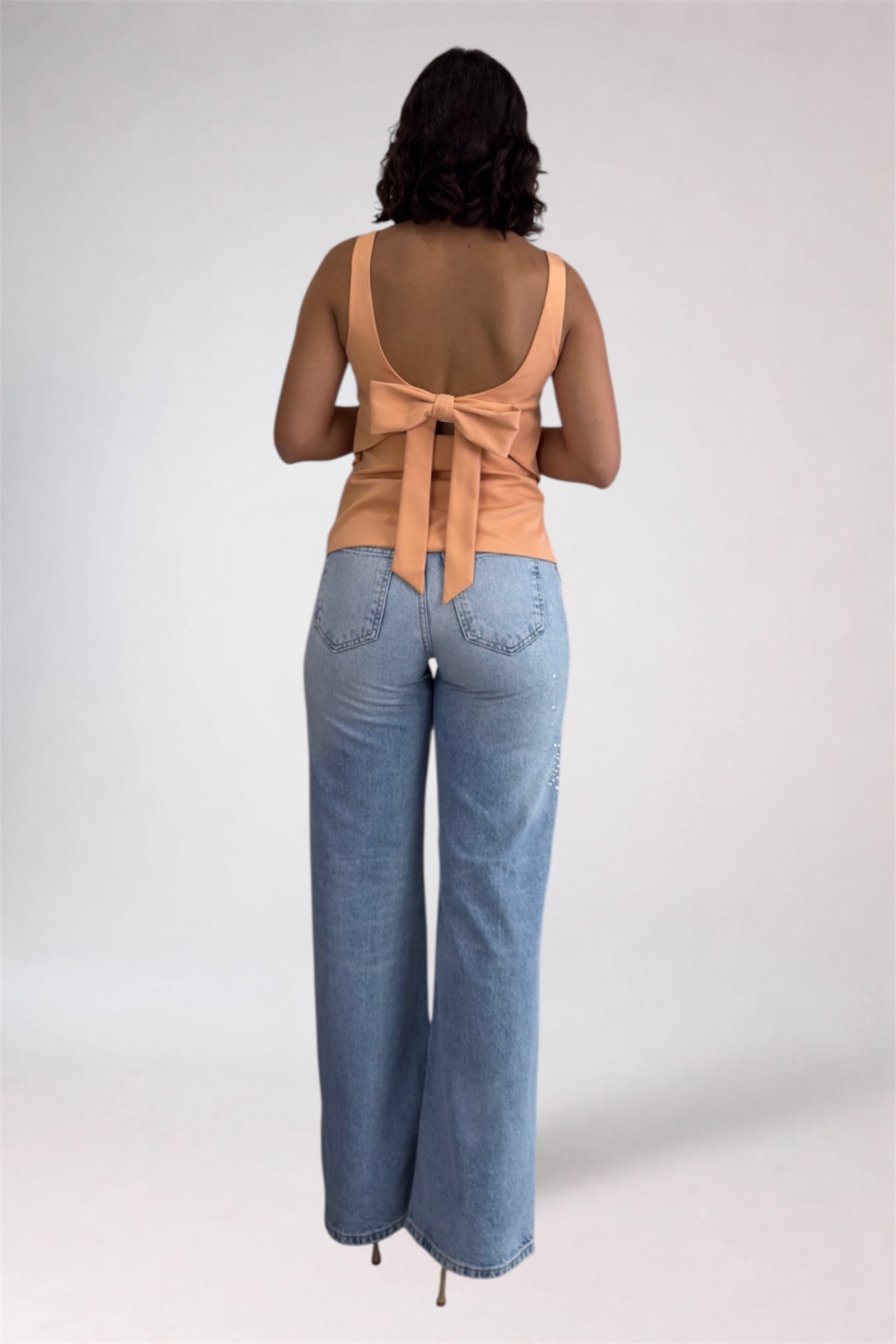 Woman wearing a beige sleeveless top with a bow and light blue jeans on a white background
