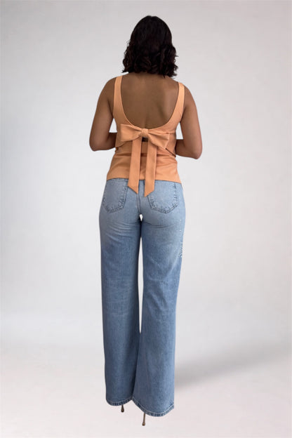 Woman wearing a beige sleeveless top with a bow and light blue jeans on a white background