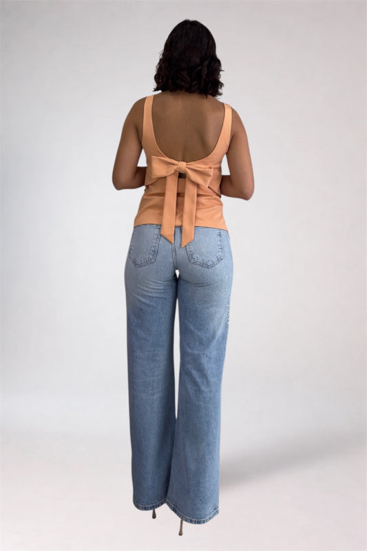 Woman wearing a beige sleeveless top with a bow and light blue jeans on a white background