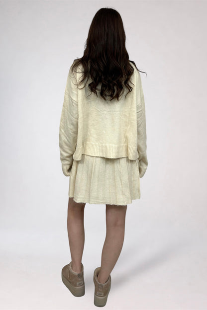 Person wearing a light-colored outfit with a sweater and skirt on a white background