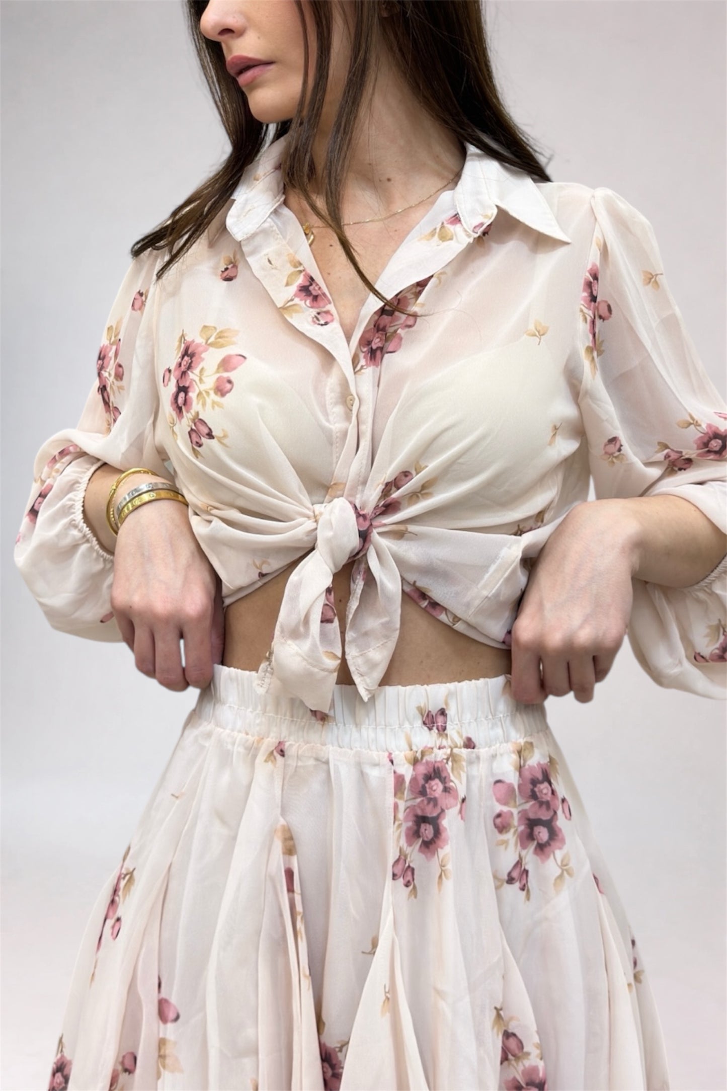 Woman wearing a floral blouse and skirt set against a plain background