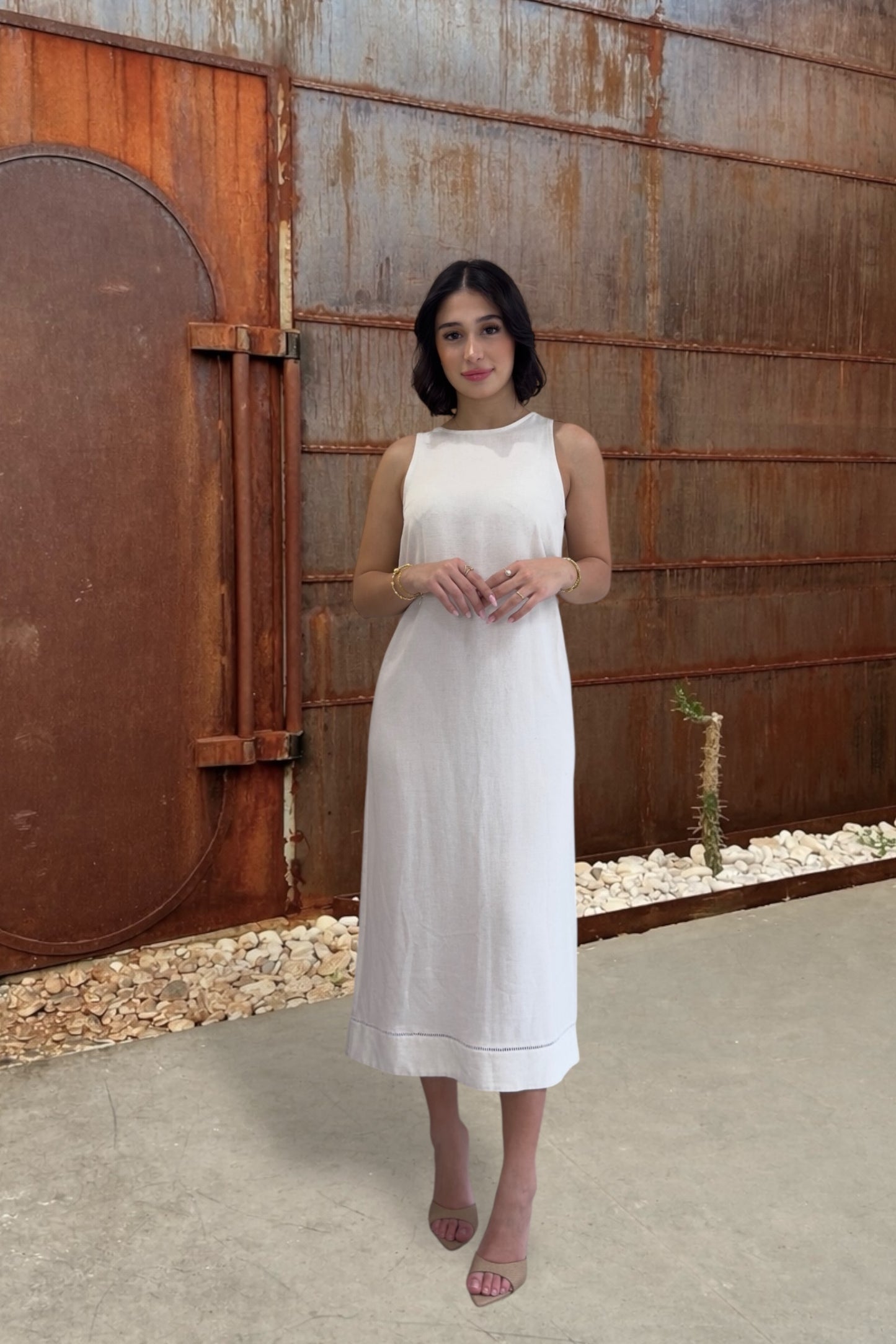 Woman in a white dress standing in front of a rusted metal wall.