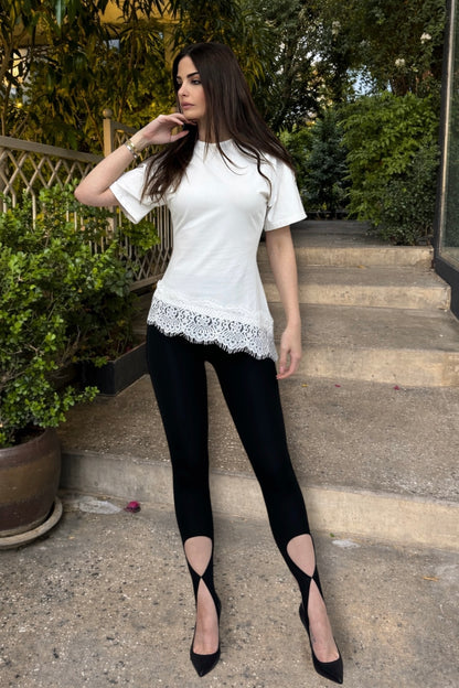 Woman wearing a white top with lace details and black pants on outdoor steps.