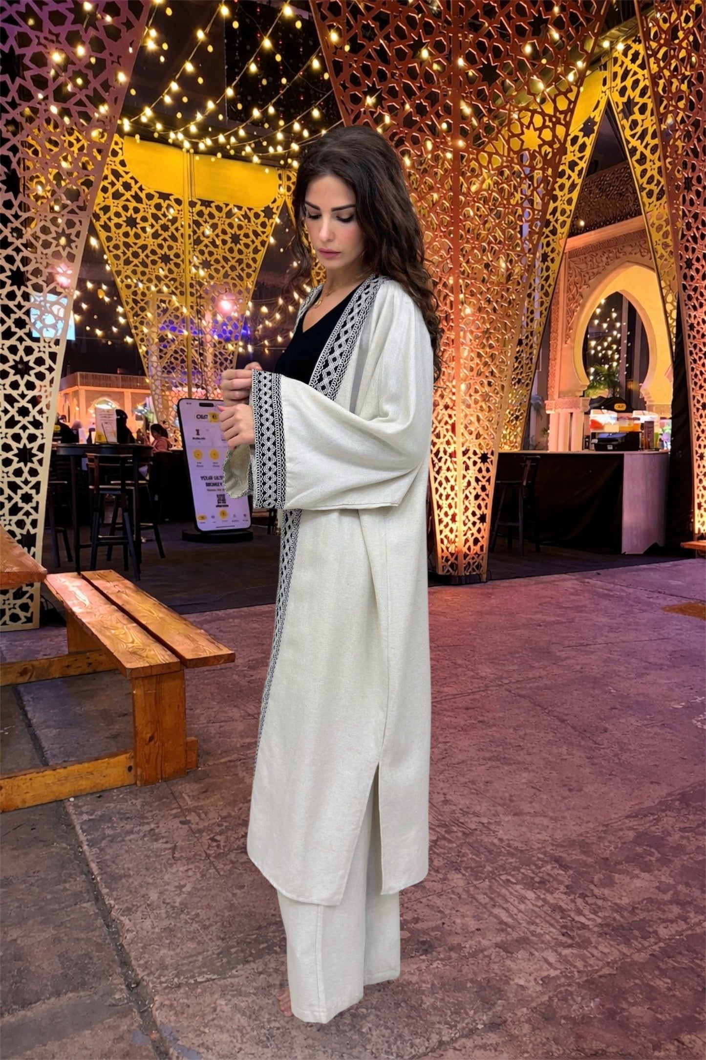 Woman in a white outfit standing in an outdoor setting with decorative lights and arches.