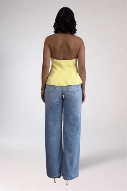 Person wearing a yellow strapless top and blue jeans on a plain background