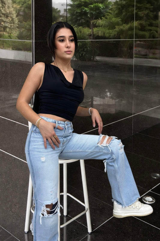 Woman sitting on a stool wearing a black top and light blue jeans in an indoor setting.