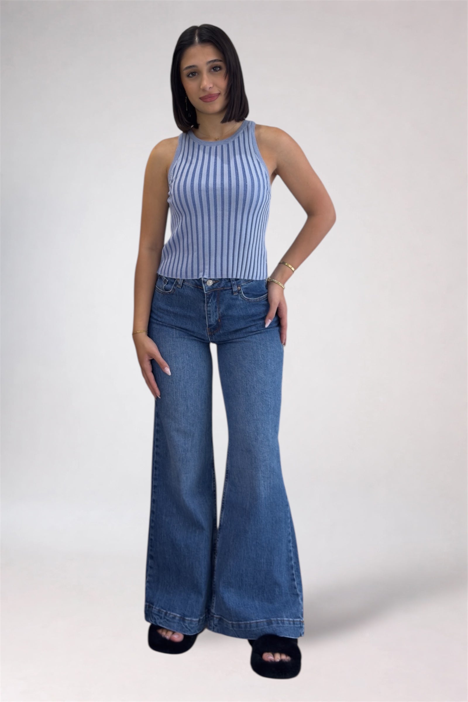 Woman wearing a striped sleeveless top and blue flared jeans on a white background