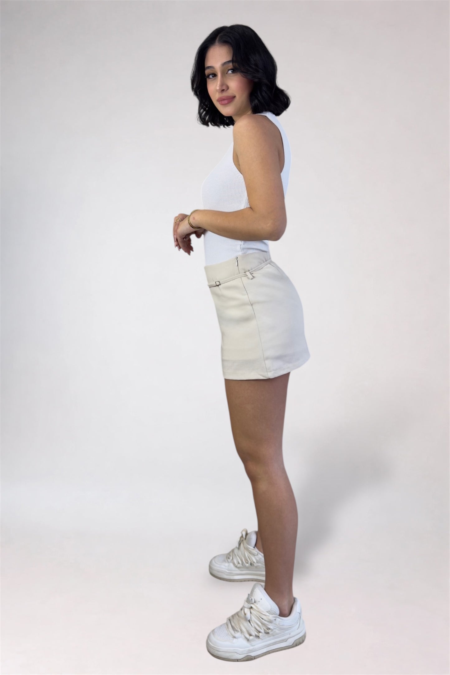 Person wearing a white tank top and shorts with white sneakers on a plain background