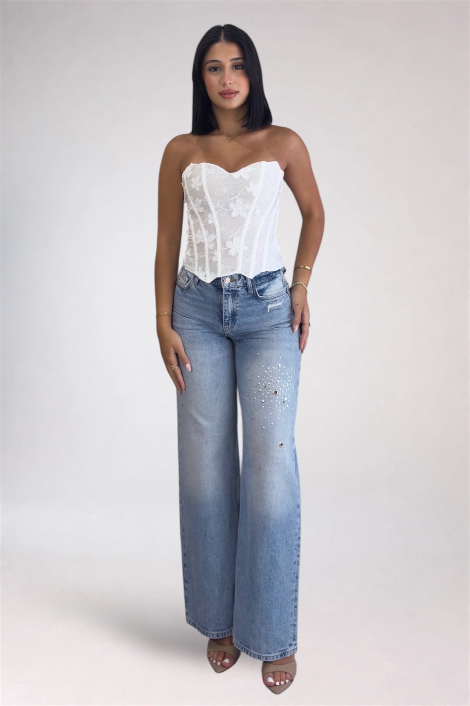 Woman wearing a white strapless top and blue jeans on a plain background