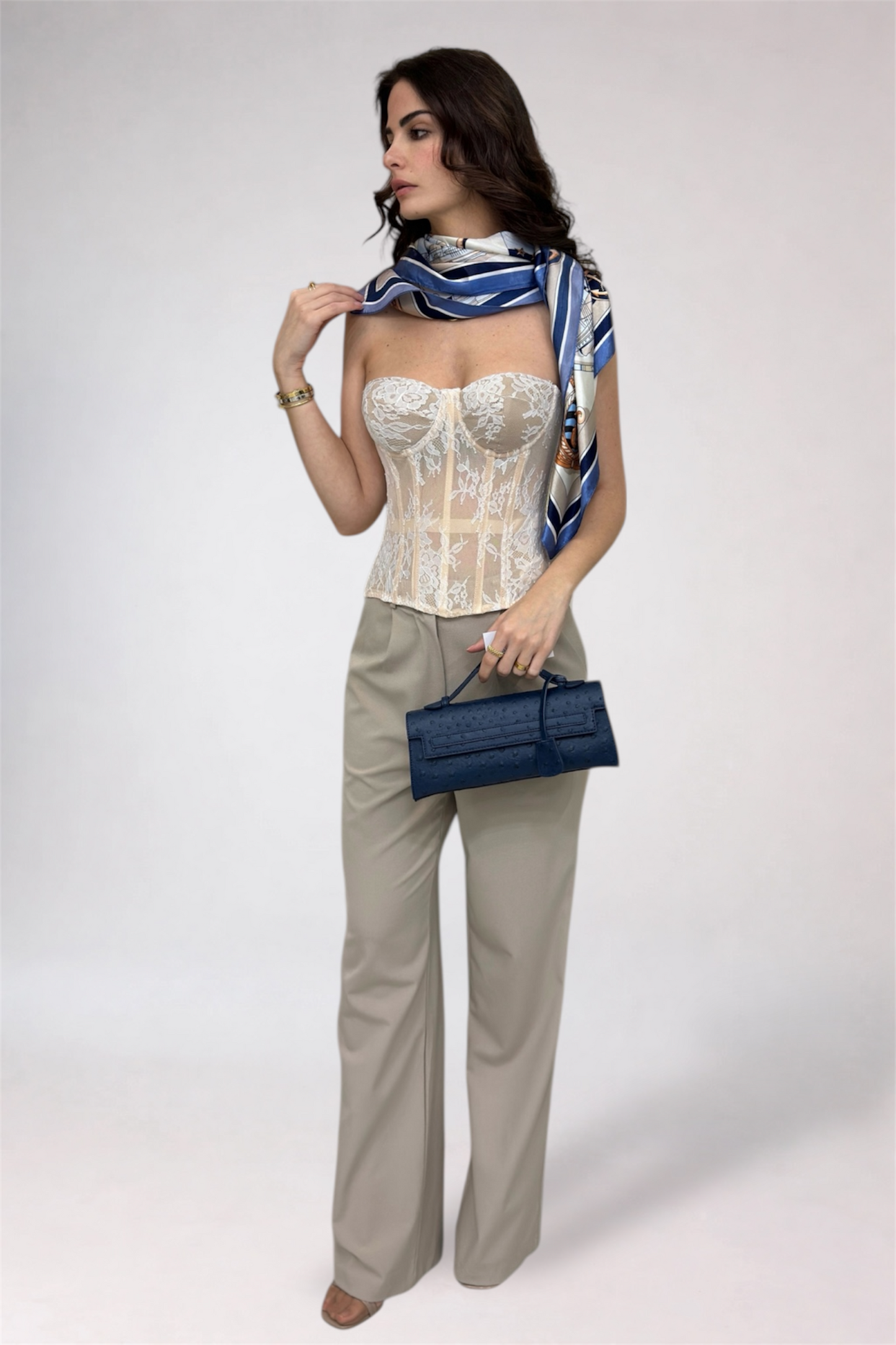 Woman wearing a white corset, beige pants, and holding a blue handbag on a white background