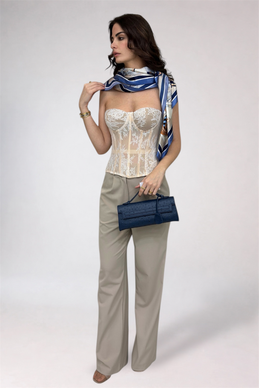 Woman wearing a white corset, beige pants, and holding a blue handbag on a white background