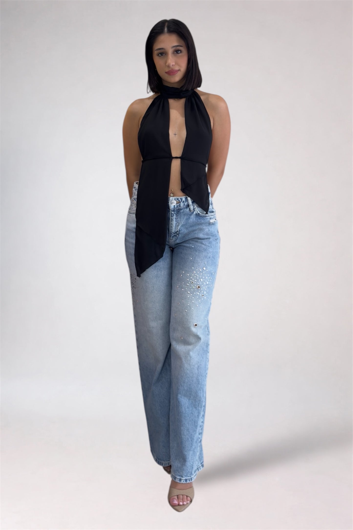 Woman wearing a black top and light blue jeans against a white background