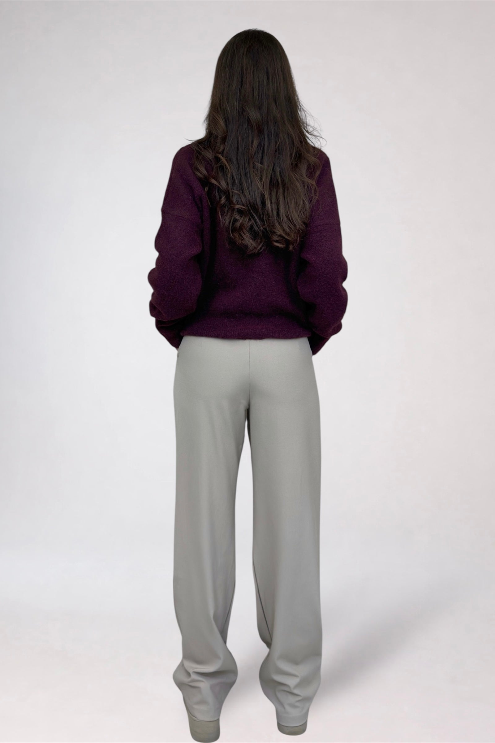 Person wearing a purple sweatshirt and gray pants on a white background