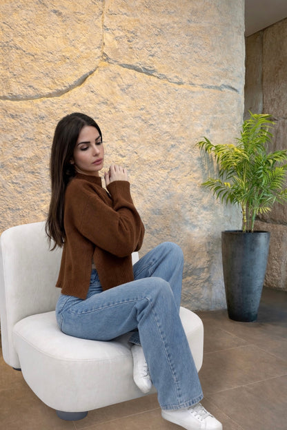 Woman sitting on a white chair in a modern indoor setting with a stone wall and plant.