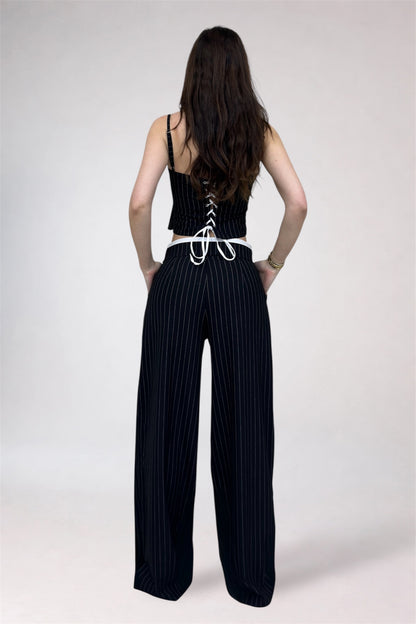Woman wearing a black lace-up top and wide-leg pants on a white background