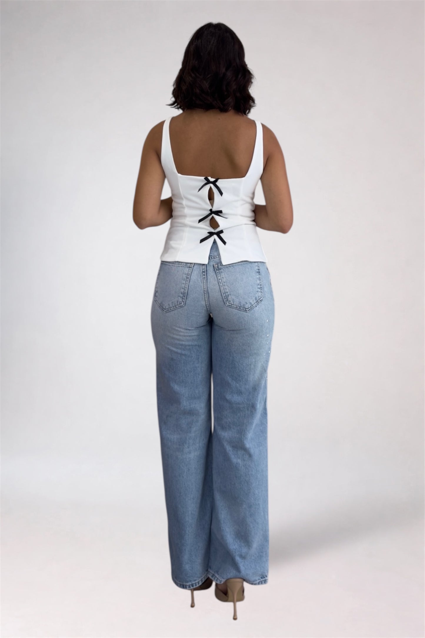 Person wearing a white lace-up top and blue jeans on a plain background
