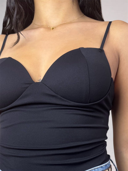 A close-up of a woman wearing a black spaghetti-strap camisole top with molded underwire cups and a ruched bust design.