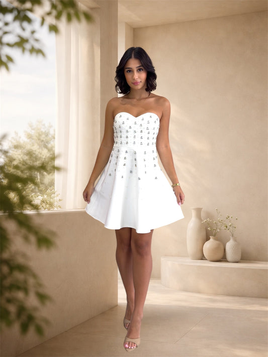 Woman in a white strapless dress standing in a bright room with large windows.