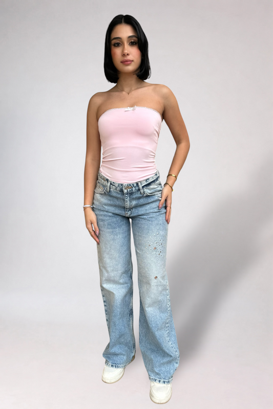 Woman wearing a pink strapless top and blue jeans on a plain background