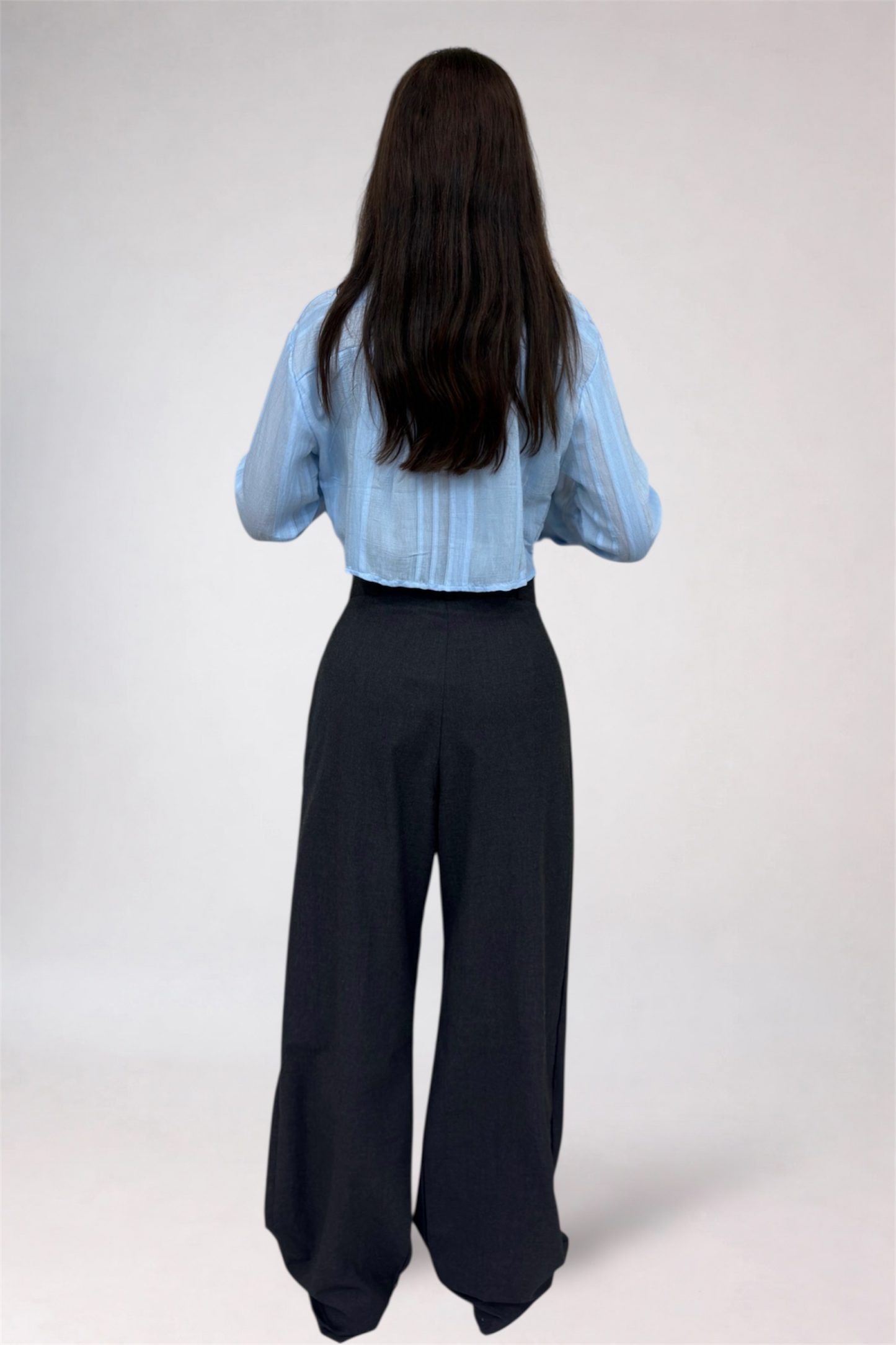 Person wearing a light blue blouse and black pants on a white background