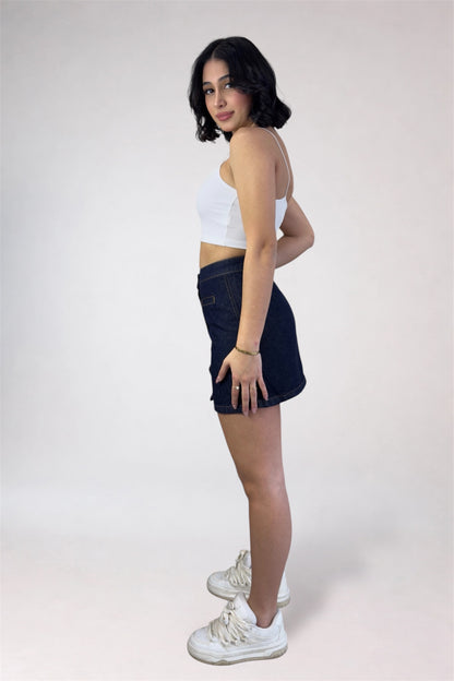 Woman wearing a white crop top and dark denim skirt with white sneakers on a plain background