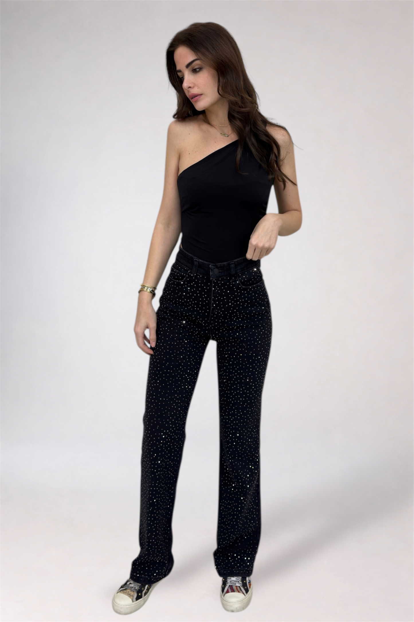 Woman wearing a black one-shoulder top and black pants with glitter on a white background