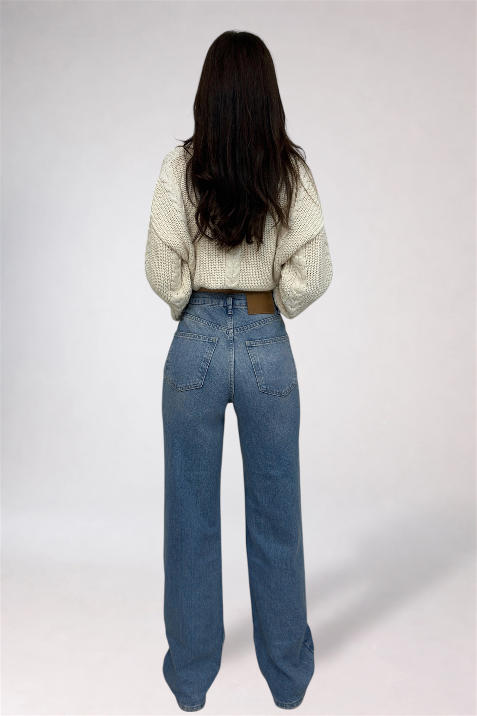 Person wearing a white textured sweater and blue jeans on a plain background