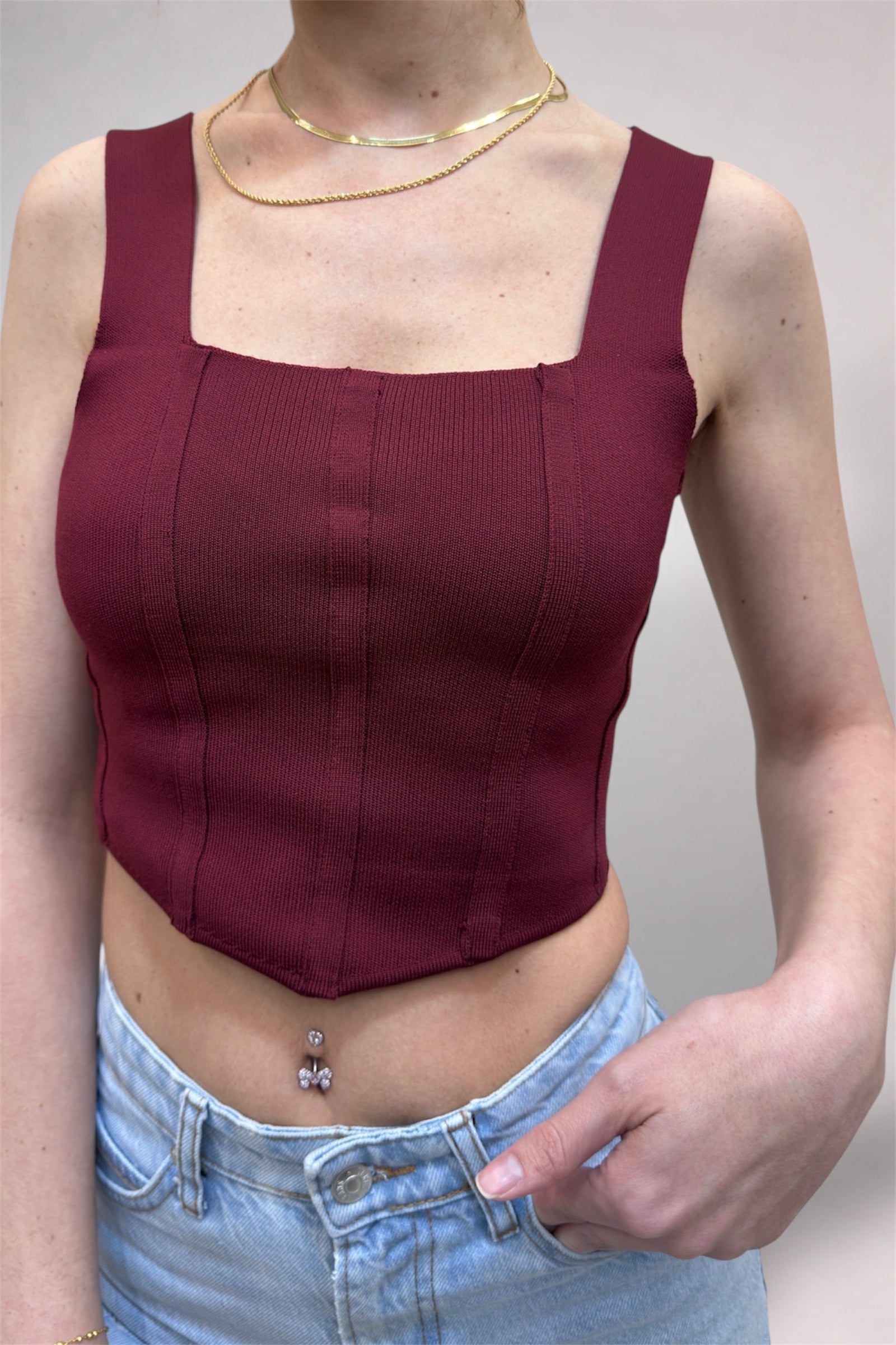 Person wearing a burgundy top and light blue jeans against a plain background