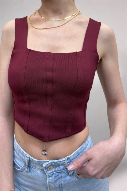 Person wearing a burgundy top and light blue jeans against a plain background