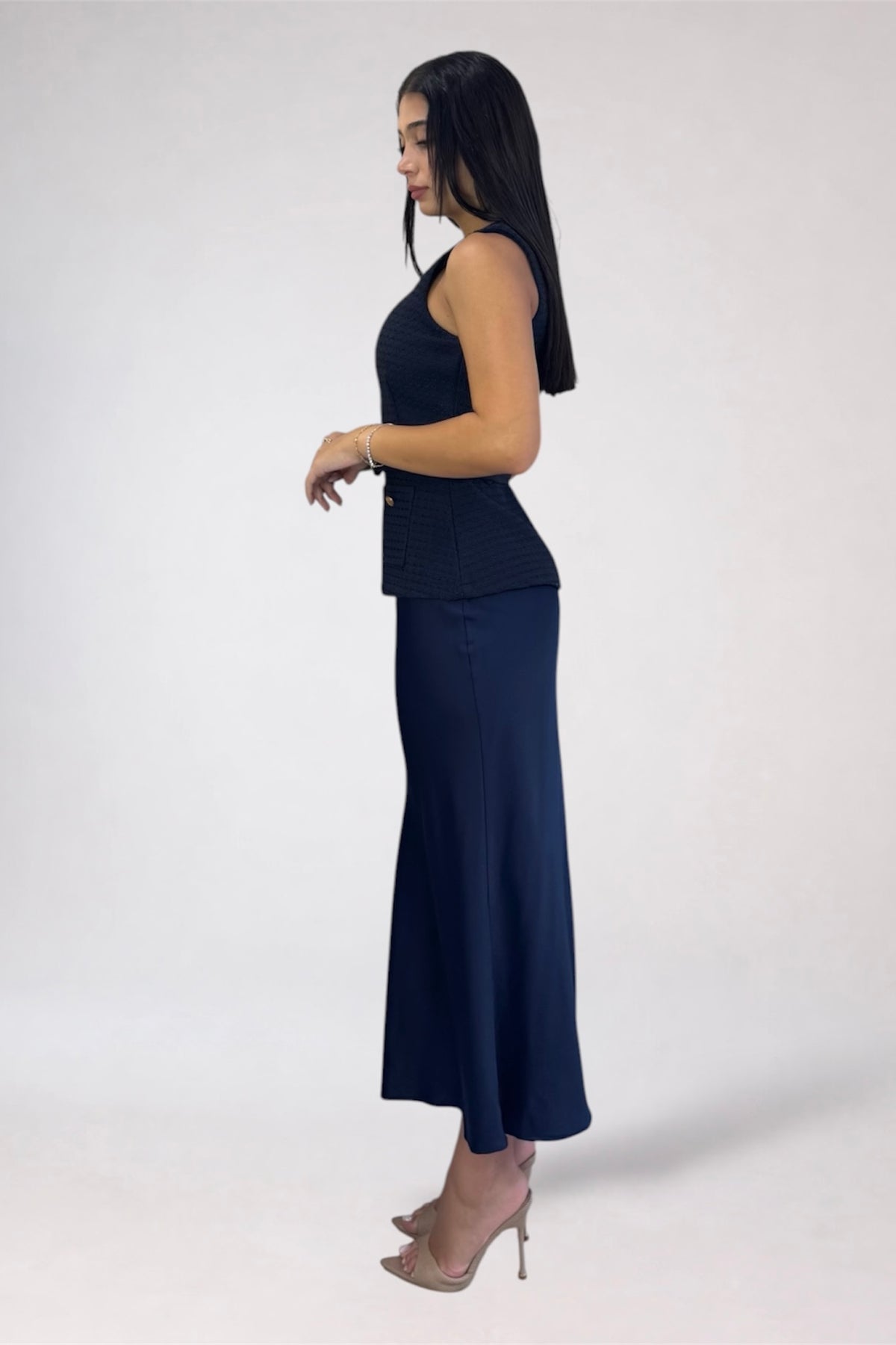 A woman modeling a dark navy sleeveless top and matching long skirt, shown in profile against a plain light gray studio background.