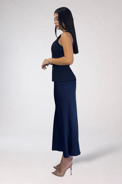 A woman modeling a dark navy sleeveless top and matching long skirt, shown in profile against a plain light gray studio background.