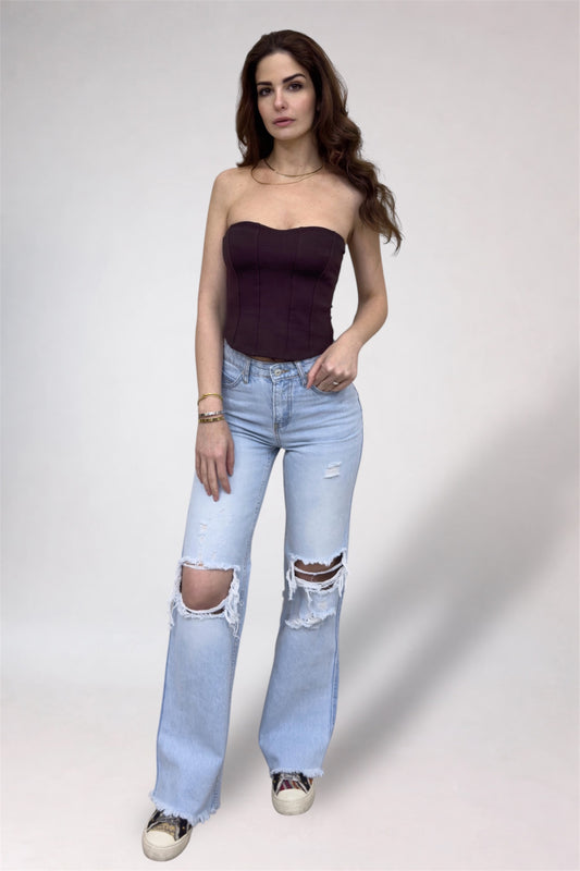 Woman wearing a strapless top and ripped jeans on a plain background