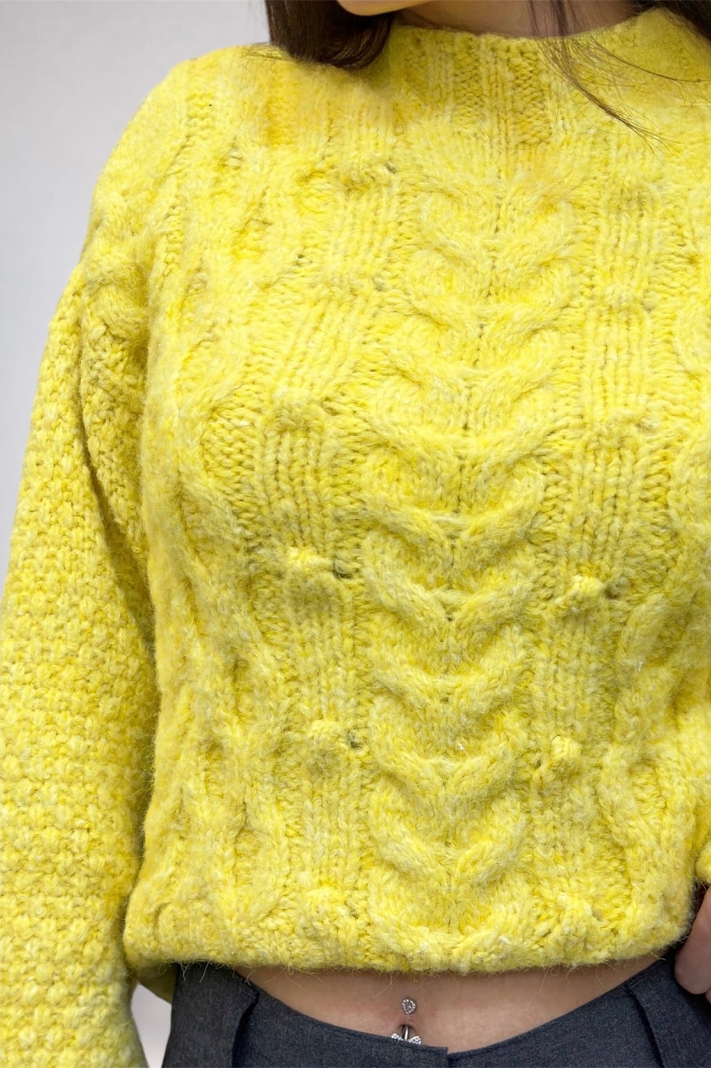 Yellow knitted sweater with cable pattern worn by a person, on a plain background