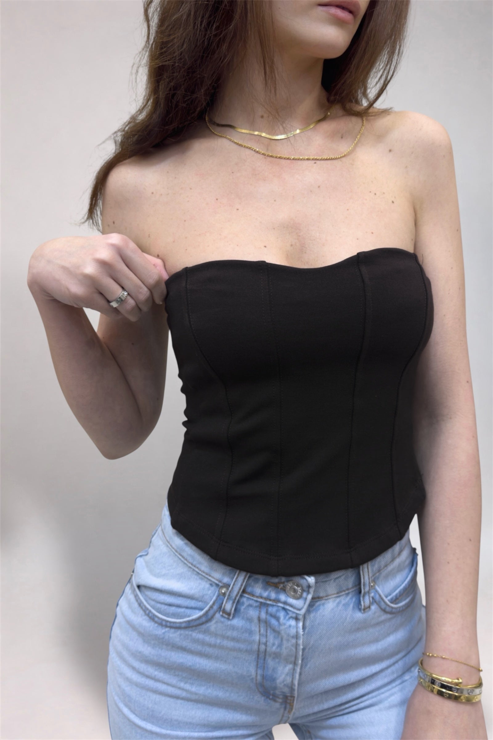 Person wearing a black strapless top and light blue jeans against a plain background