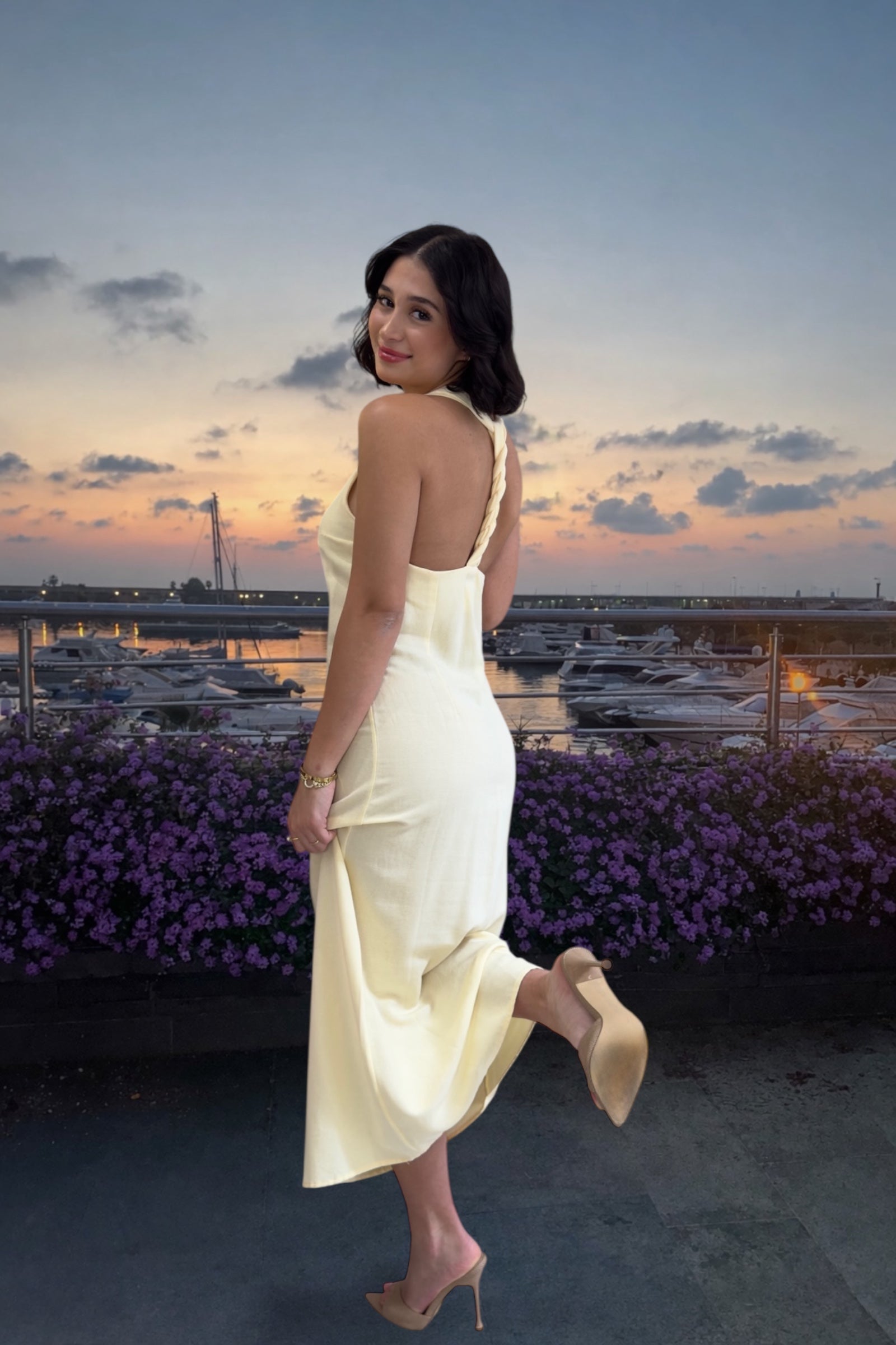 Woman in a white dress standing on a rooftop with a cityscape and sunset in the background
