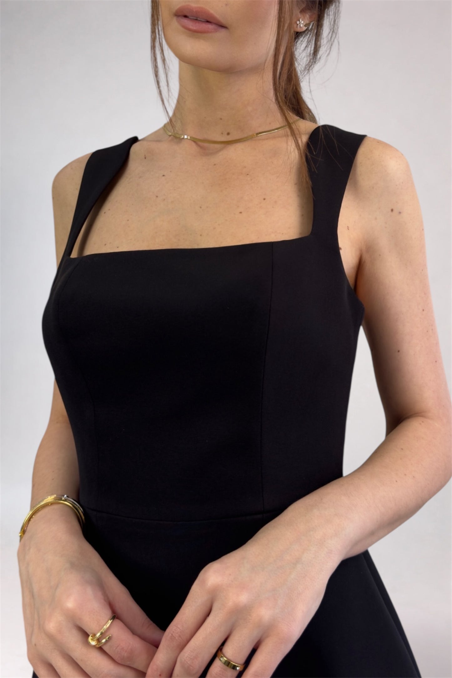 Woman wearing a black sleeveless dress against a plain background
