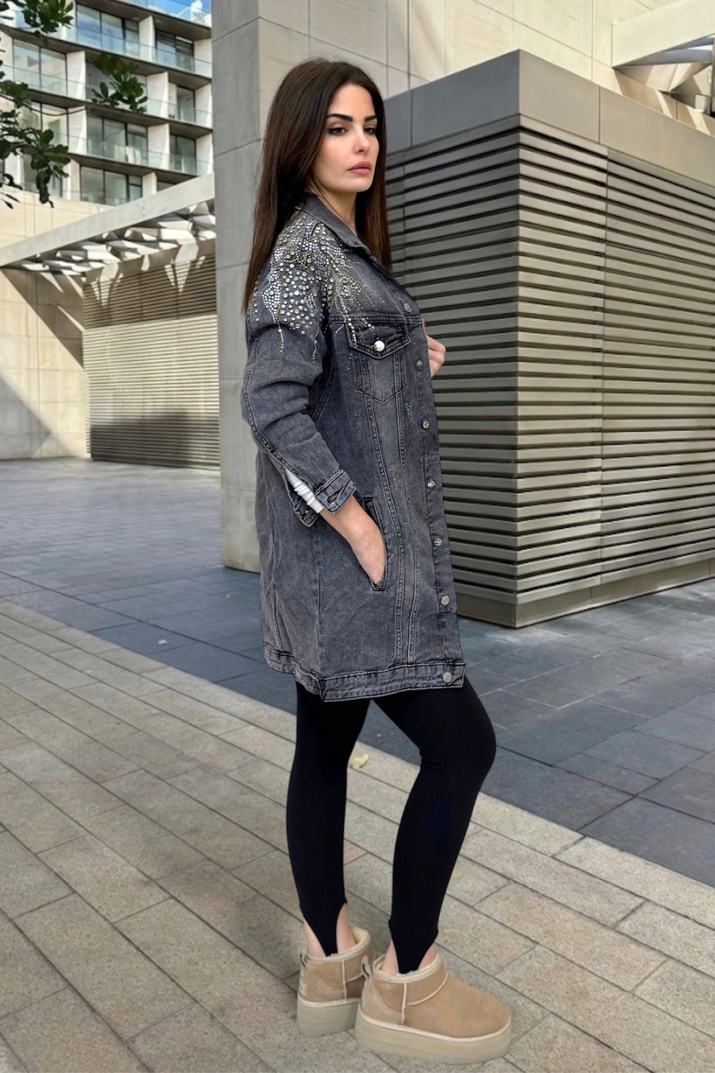 Woman wearing a denim jacket with decorative elements, black leggings, and beige shoes on a city street.