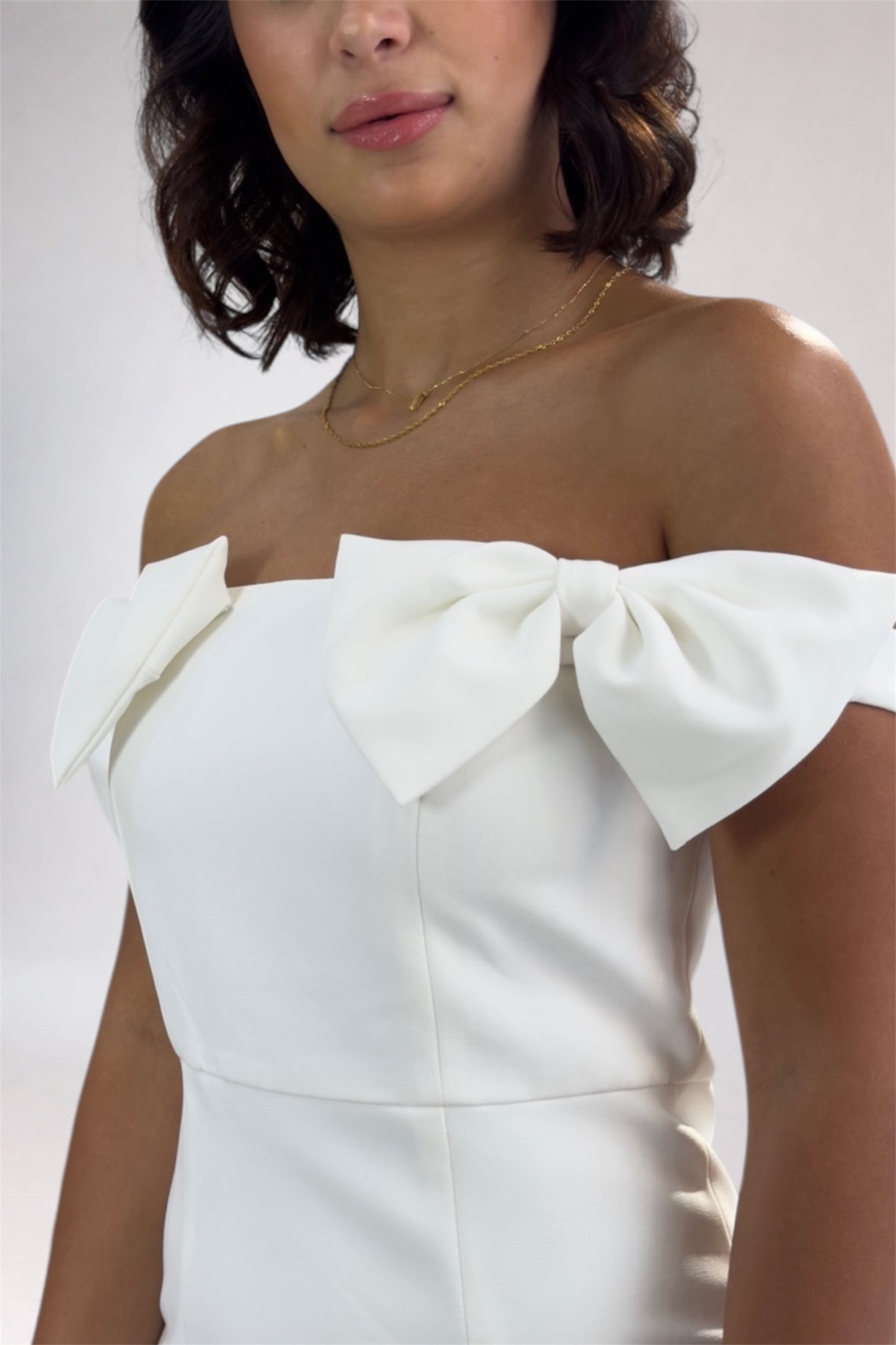 White off-shoulder dress with bow details on a plain background