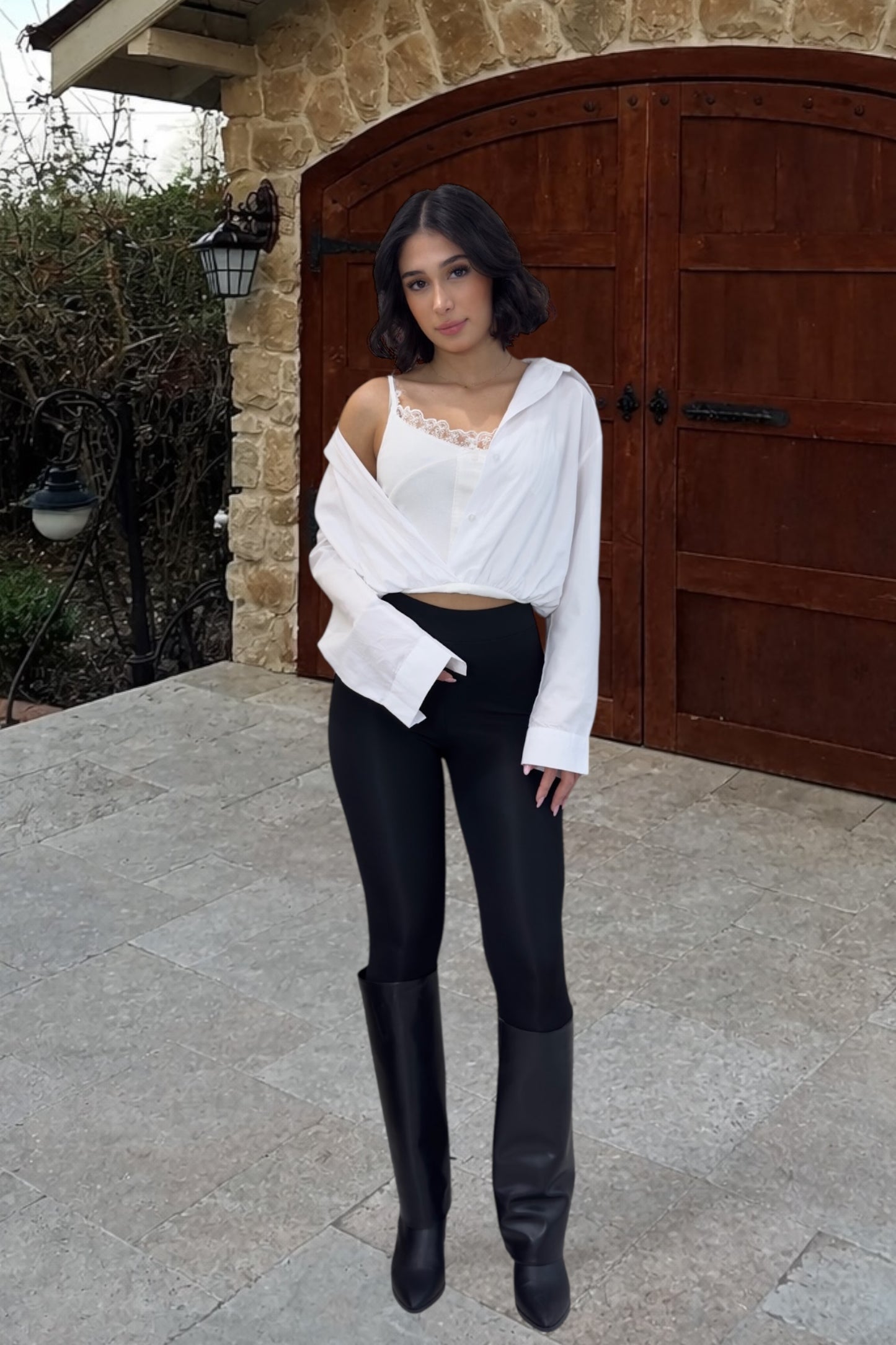 Woman in white top and black pants standing in front of a stone building with wooden doors.