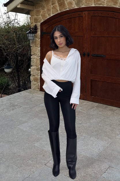 Woman in white top and black pants standing in front of a stone building with wooden doors.