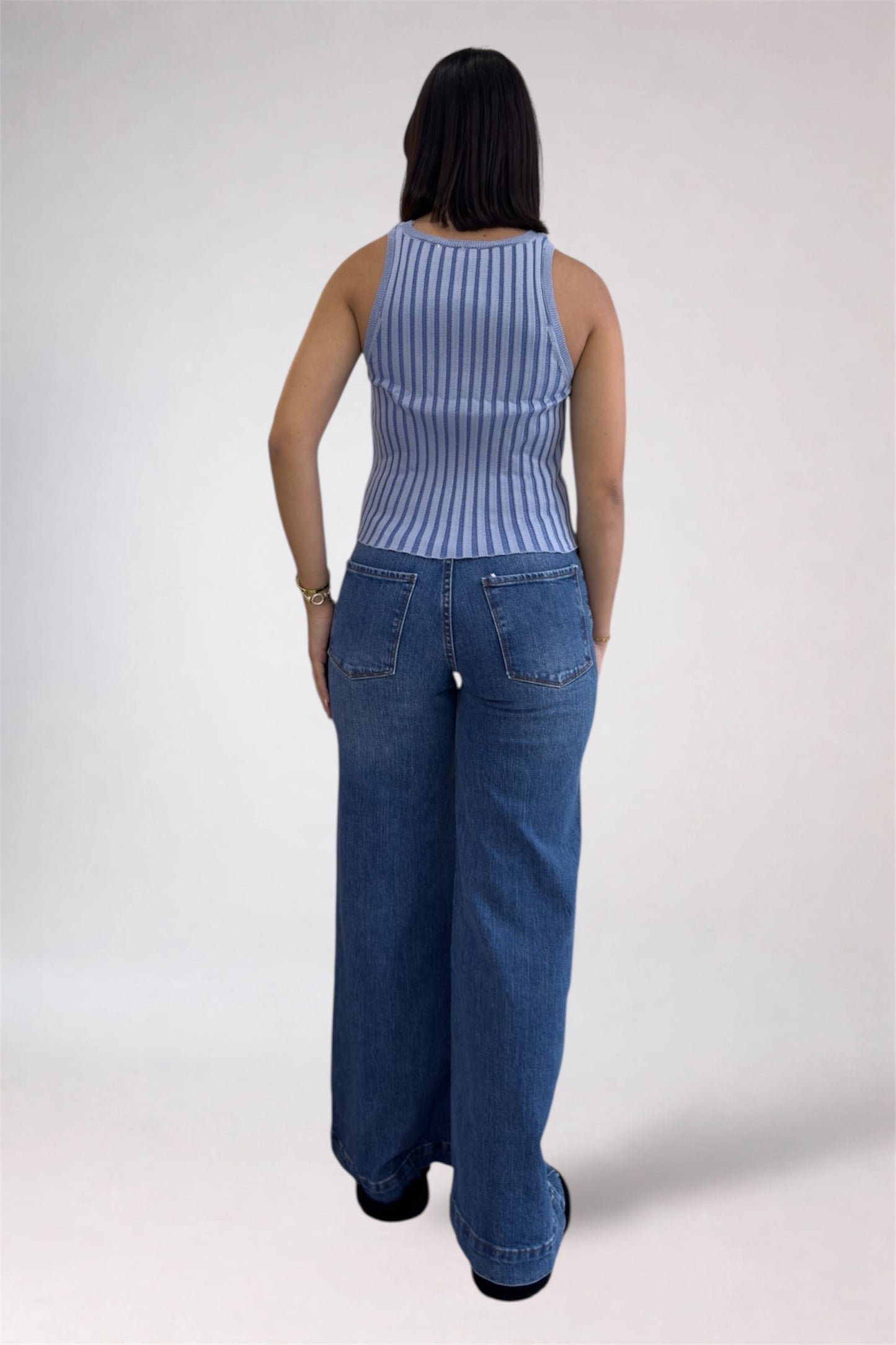 Person wearing a blue striped sleeveless top and wide-leg jeans on a white background