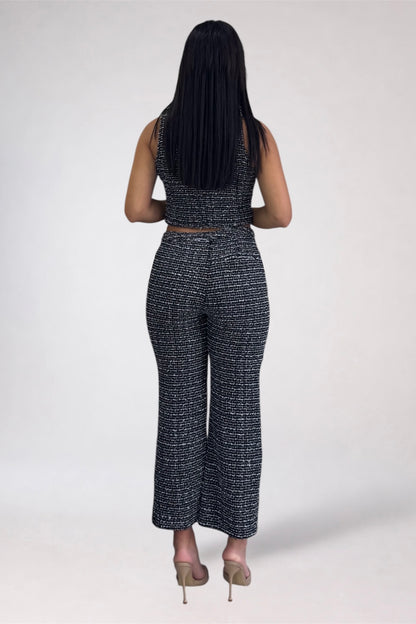 A woman viewed from behind wearing a matching sleeveless crop top and wide-leg pants set in a black and white textured tweed pattern, paired with beige high heels, against a light gray studio background.