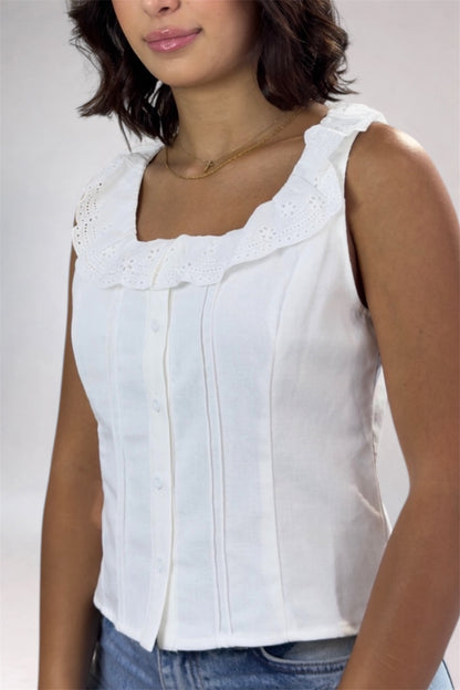 Woman wearing a white sleeveless top with lace details on a plain background