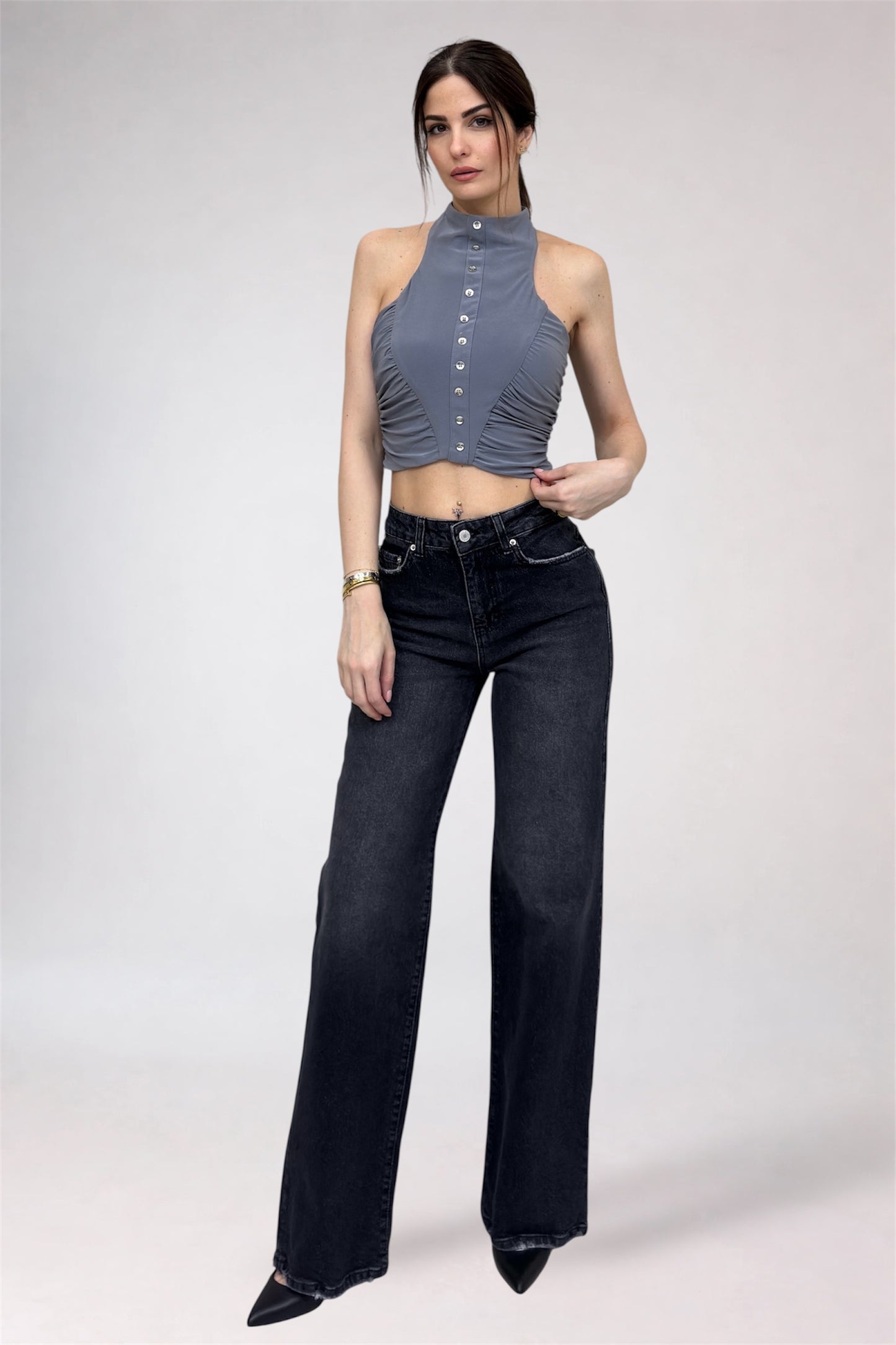 Woman wearing a gray halter top and black high-waisted jeans on a white background