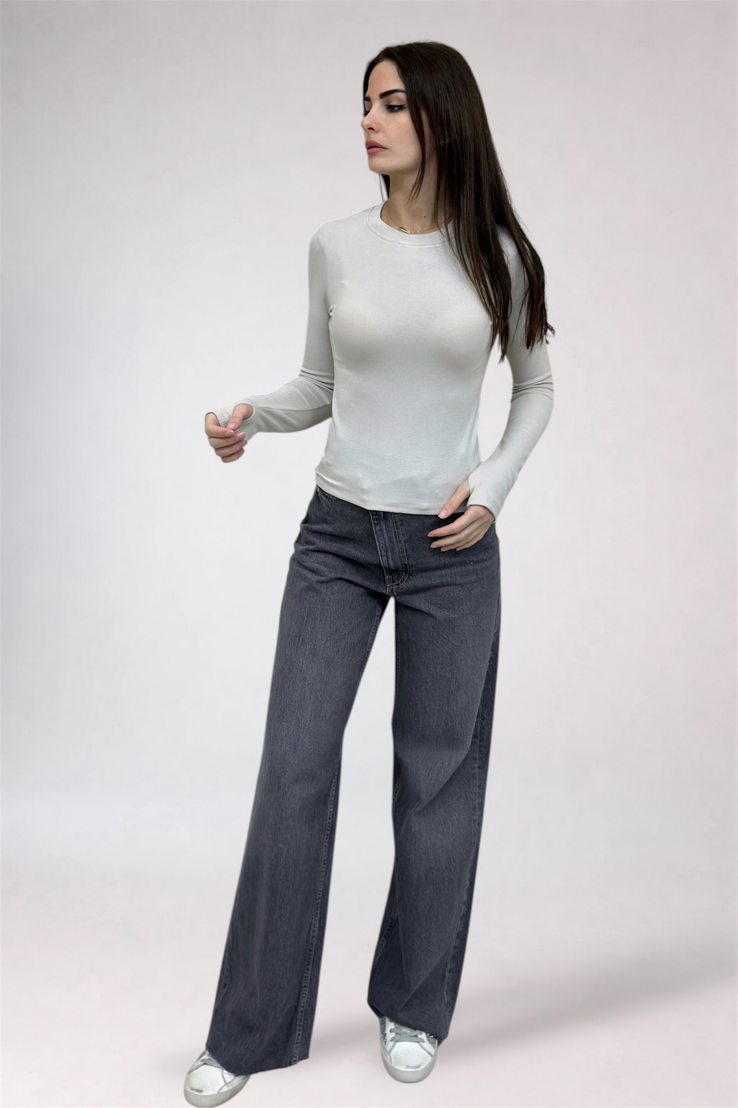 Woman wearing a white long-sleeve top and dark gray wide-leg jeans on a light gray background