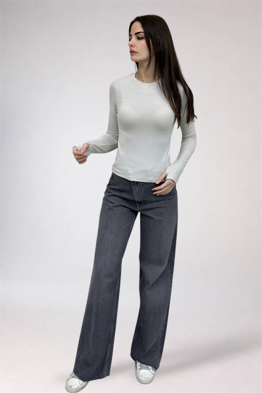 Woman wearing a white long-sleeve top and dark gray wide-leg jeans on a light gray background