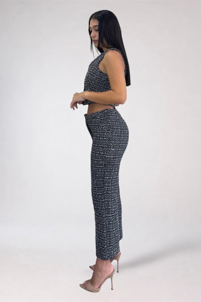 A woman modeling a matching two-piece knit set featuring a halter crop top and high-waisted wide-leg pants, both in a black and white textured tweed pattern, paired with nude high heels against a plain white studio background.