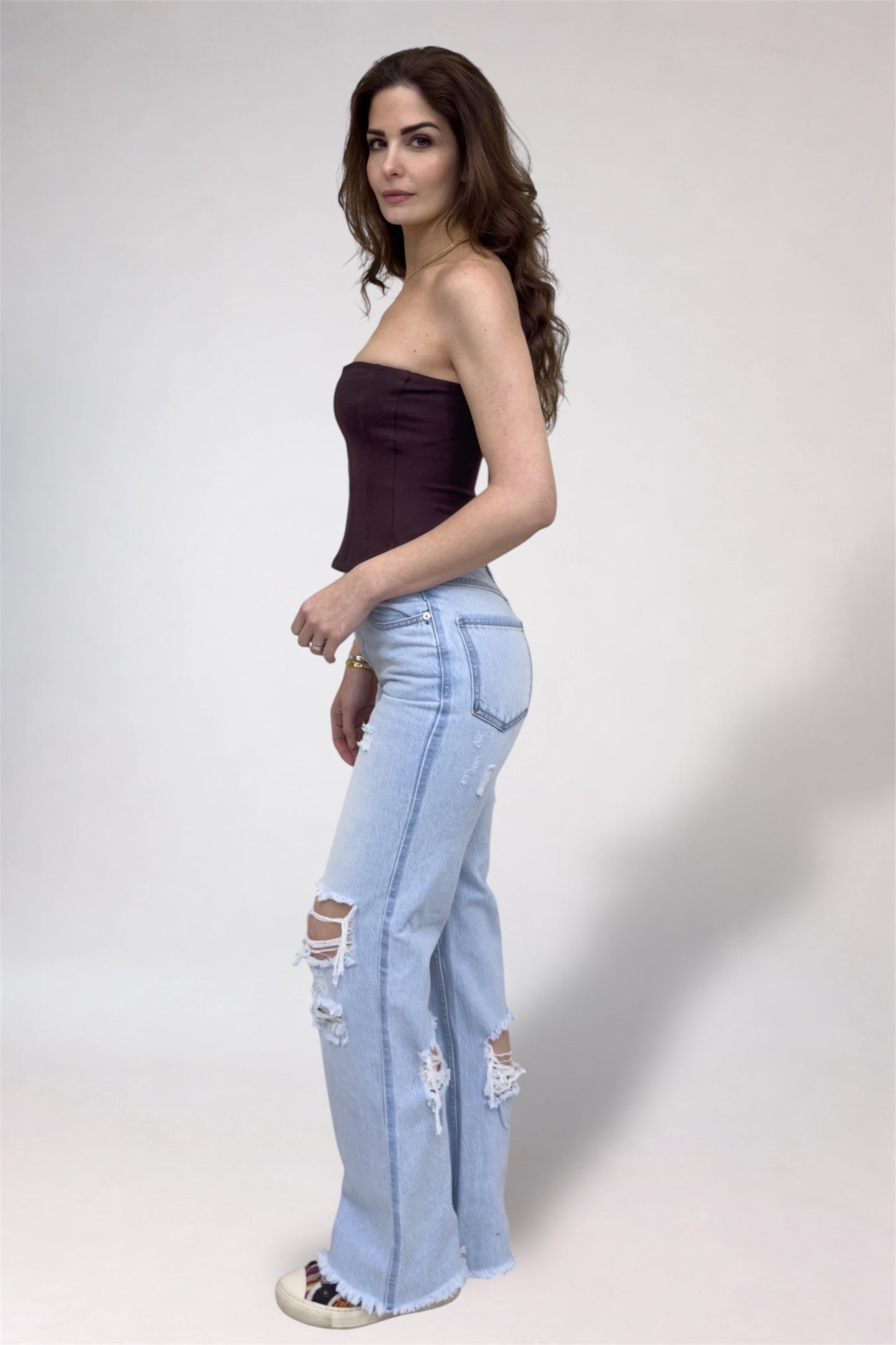 Woman wearing a strapless top and light blue ripped jeans on a white background