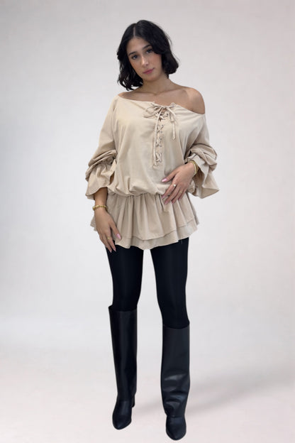 Woman wearing a beige off-shoulder top and black leggings with knee-high boots on a white background